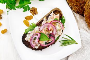 Salmon, petiole celery, raisins, walnuts, red onions and curd cheese salad on toasted bread with green lettuce on a plate on a wooden board background from above