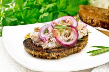 Salad of salmon, petiole celery, raisins, walnuts, red onions and cottage cheese on toasted bread with green lettuce on a plate on wooden board background