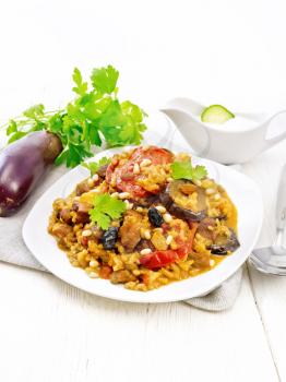 Eastern and European national dish of maklube made of rice, eggplant, tomatoes, spices and garlic in a plate on a towel on background of white wooden board