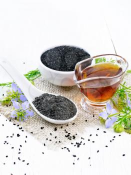 Flour Nigella sativa in a spoon, black cumin seeds in a bowl and oil in gravy boat on burlap, sprigs of kalingi with blue flowers and green leaves on light wooden board background