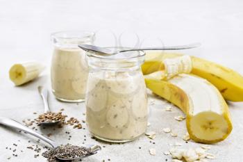 Milkshake with chia seeds, flax seeds, oatmeal, puffed rice and banana in two glass jars on a granite table background