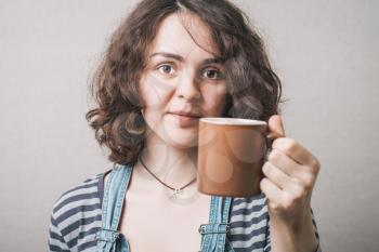 A woman offers a cup of coffee or tea. Gray background