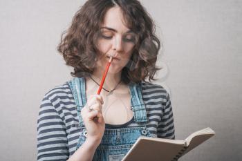 woman writes in a notebook, dressed in overalls