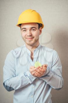 Young guy in a helmet holding a house made of paper. 