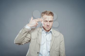 young businessman doing suicide symbol on gray.  businessman shooting his own head with his fingers