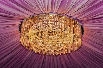 Golden chandelier with violet curtain, closeup view
