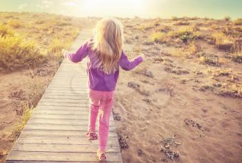 Little girl goes by boardwalk in sea shore at sunrise