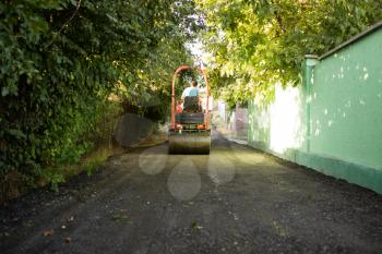 heavy machine rolls a new asphalt road .