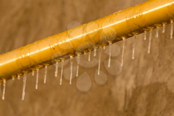 Icicles on a yellow pipe at sunset .