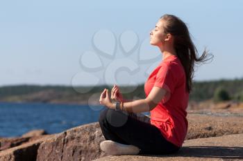 Young Woman sitting in lotus position on rock by the sea