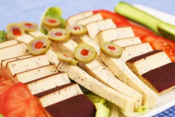 Cheese, olives and vegetables on plate.