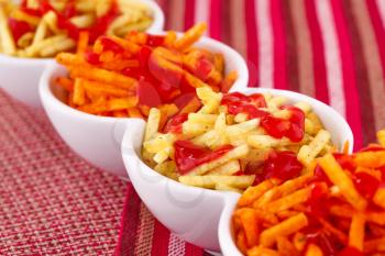 Potato chips with ketchup isolated on colorful tablecloth.