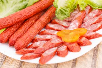 Fresh sausages and green salad leaves in plate on bamboo mat background.