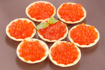 Red caviar in round pastries on brown plate.