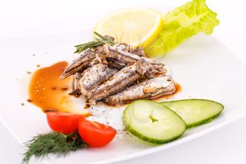 Fish, vegetables and lemon on white plate.