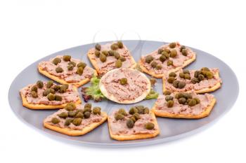 Meat pate with capers on crackers and lettuce on plate isolated on white background.
