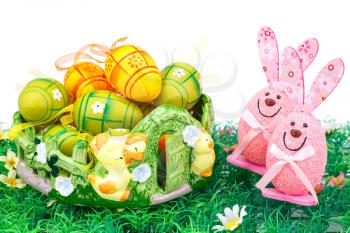 Easter decoration with colorful eggs in basket and bunnies on artificial grass.