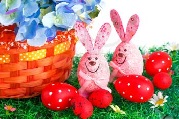 Easter decoration with bunnies, eggs and flowers in basket on artificial grass.
