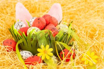 Easter decoration with colorful eggs in basket, ribbons, straw and bunny ears.