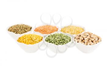 The collection of different groats in the white ceramic bowls isolated on a white background. Split peas, colorful lentils, chickpeas.
