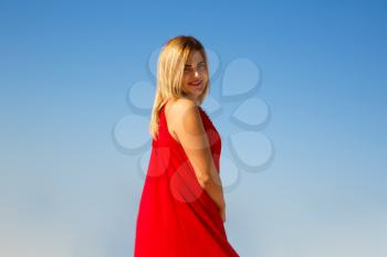 Blond woman in the red dress on the blue sky background.