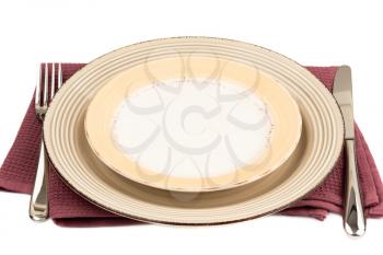 Two empty plates, knife and fork on purple cotton towel on white background.