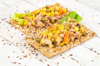 Sandwiches with crackers, tuna fish, corn, and carrot on gray wooden background.