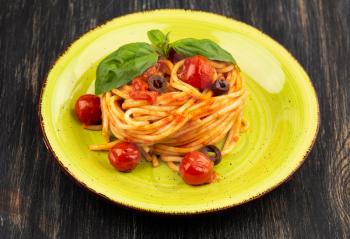 Pasta spaghetti Napoli or Napolitana on green plate on black background. Italian cuisine.