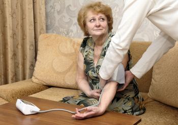 Old woman measures arterial pressure , with doctor helps.