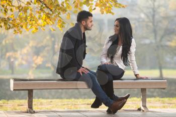 Young Couple Sitting On A Bench In The Beautiful Autumn Day