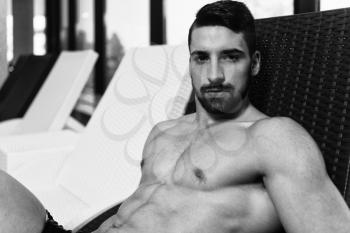 Young Man Resting On Sun Loungers By Swimming Pool And Flexing Muscles