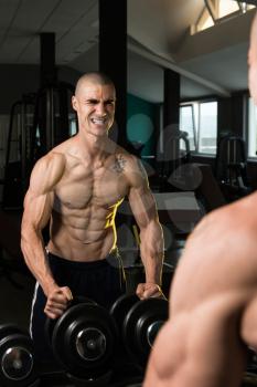 Young Man Standing Strong In Front Of A Mirror And Flexing Muscles - Muscular Athletic Bodybuilder Fitness Model Posing After Exercises