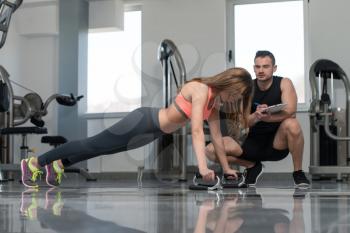 Personal Trainer Takes Notes While Young Woman Exercise Push-Up Strength In A Gym