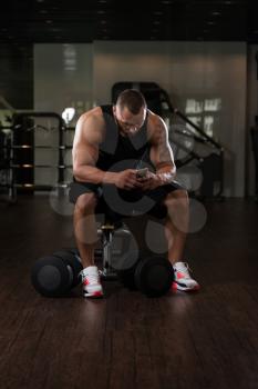 Bodybuilding Healthy Fitness Man Using Smartphone While Resting In The Gym