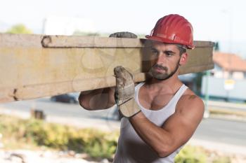 Smiling Carpenter Carrying A Large Wood Plank On His Shoulder