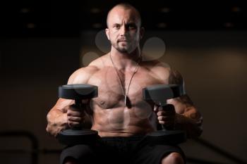 Portrait Of A Muscular Man Resting On The Bench In Fitness Gym With Dumbbells
