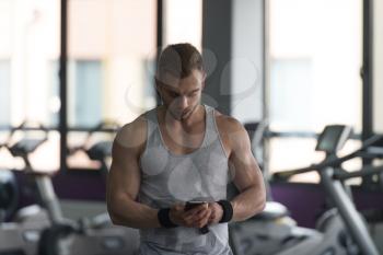 Healthy Fitness Man Using Smartphone While Resting In The Gym