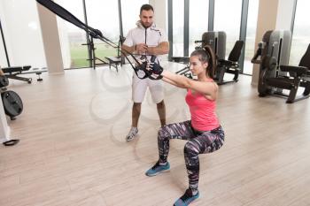 Personal Trainer Showing Young Woman How To Train With Trx Fitness Straps In The Gym