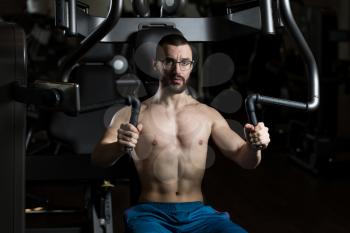 Handsome Muscular Fitness Man Wearing Glasses Doing Heavy Weight Exercise For Chest On Machine With Cable In The Gym
