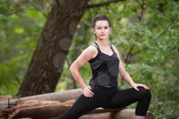 Young Woman Stretching Before Running In Wooded Forest Area - Training And Exercising For Trail Run Marathon Endurance - Fitness Healthy Lifestyle Concept