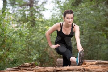 Young Woman Stretching Before Running In Wooded Forest Area - Training And Exercising For Trail Run Marathon Endurance - Fitness Healthy Lifestyle Concept