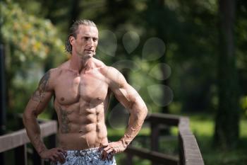 Healthy Mature Tattoo Man Standing Strong Outdoors In Nature And Flexing Muscles - Muscular Athletic Bodybuilder Fitness Model Posing After Exercises