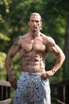 Healthy Mature Tattoo Man Standing Strong Outdoors In Nature And Flexing Muscles - Muscular Athletic Bodybuilder Fitness Model Posing After Exercises
