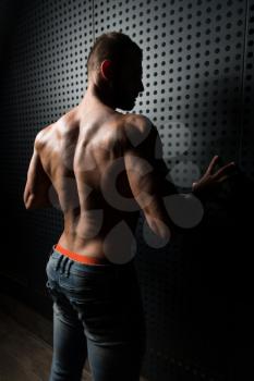 Healthy Young Man Standing Strong Standing Against a Wall and Flexing Muscles While Wearing Blue Jeans - Muscular Athletic Bodybuilder Fitness Model Posing After Exercises - a Place for Your Text
