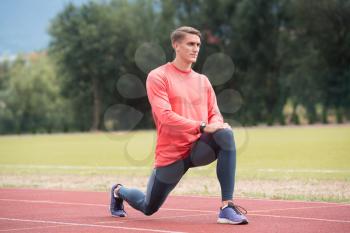 Sporty Man Stretching and Warming Up Legs for Running Fitness Workout on Track Exercising Outside