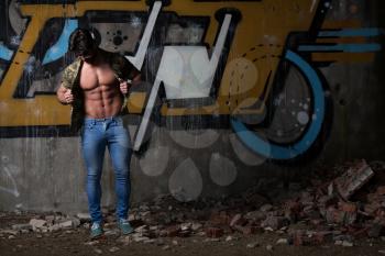 Portrait of a Young Physically Fit Man in Army Shirt Showing His Well Trained Body - Muscular Athletic Bodybuilder Fitness Model Posing After Exercises In Front Of A Graffiti Wall