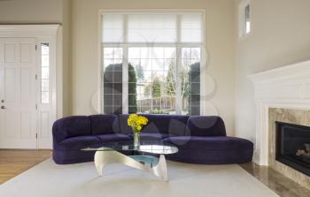 Large family living room with suede sofa, glass table in front of large double pane window with daylight coming in to room