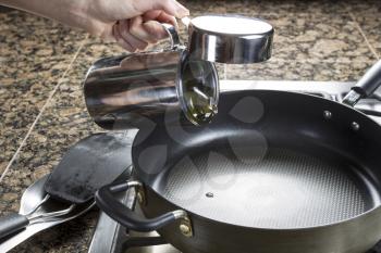 Photo of female hand adding cooking oil to frying pan in preparation of making breakfast