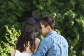 Horizontal photo of a young adult couple touching forehead to forehead with green trees in background