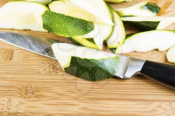 Horizontal photo of a large knife and sliced pieces of zucchini on natural bamboo cutting board